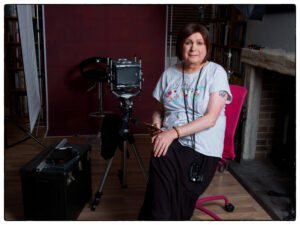 Chrissie Beckett, a woman with dark hair that frames her face sits next to a camera.