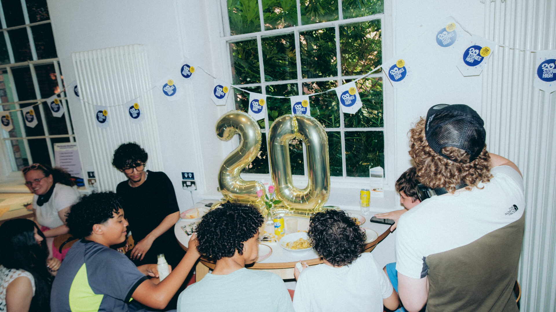 Group of people eating snacks at a table with number '20' balloons on a table