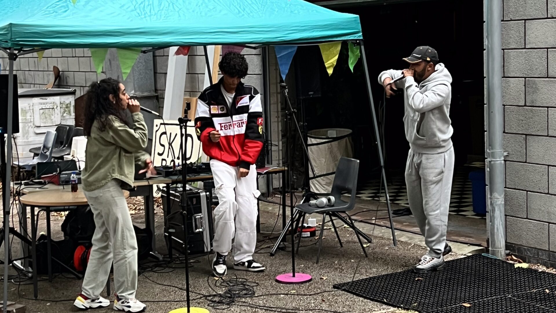 People by a gazeebo singing, with bunting across a garden