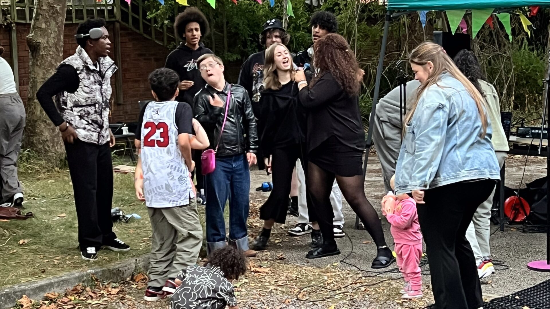 People by a gazeebo dancing and singing, with bunting across a garden