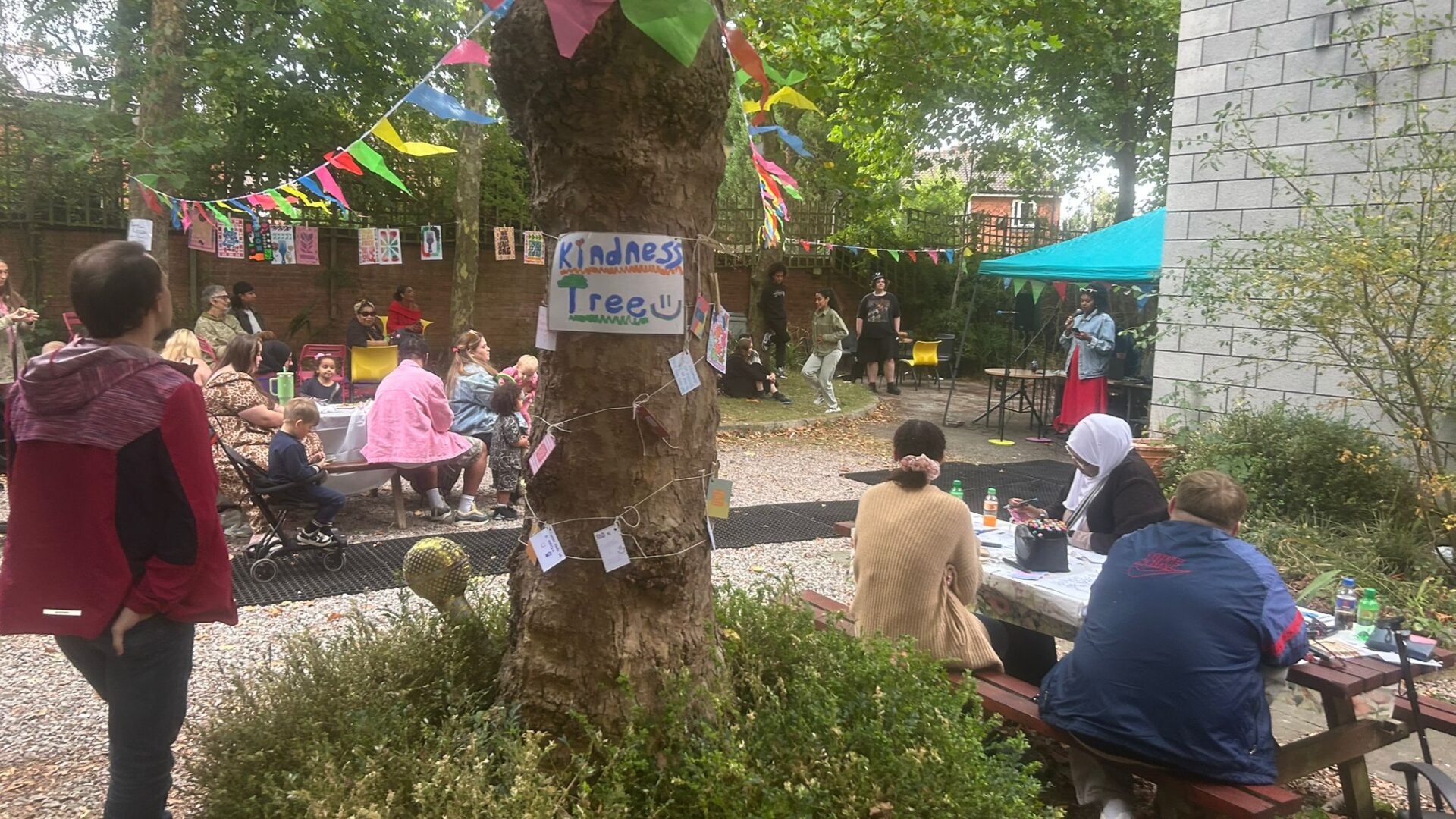 A Tree with 'kindness tree' written on it and bunting across a garden